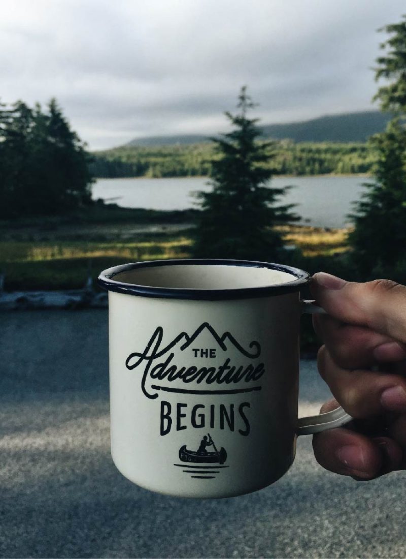 mountains in the background of a coffee cup that says the adventure begins